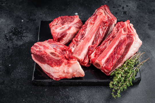 Raw beef short ribs chunks with rich meat and bone texture on slate. Minimal dark background for stew broth and slow cooking.