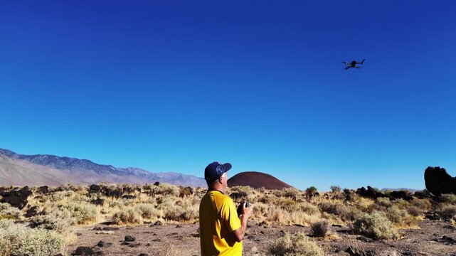 A UAV Drone flying over the Fossil Falls Crevice with the drone in view as it flies by over the cliff and the Obsidian Rocks with the pilot operating and the drone in sight