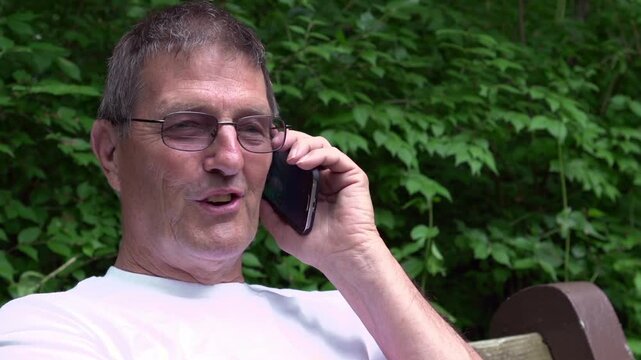 Elderly man laughing on cell phone in nature
