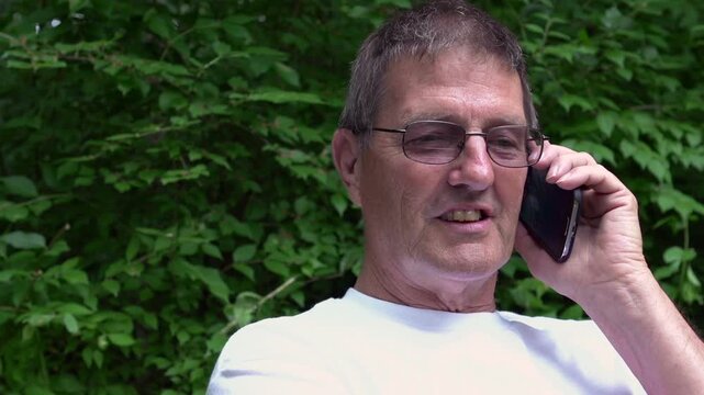 Elderly man finishes phone conversation on park bench
