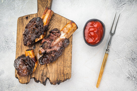 Braised beef ribs with pulled texture and caramelized surface on cutting board. Slow cooked beef ribs with plate and back ribs look.