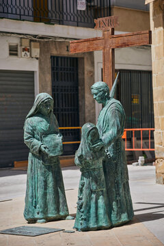 Bronze religious sculpture group beneath an INRI cross depicting three robed figures in a public space in Baeza, Andalusia, Spain