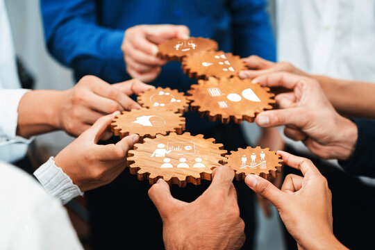 Collaborative Teamwork: Diverse Hands Connecting Wooden Gears with Icons Symbolizing Ideas, Communication, and Partnership in a Modern Office Setting. Amity