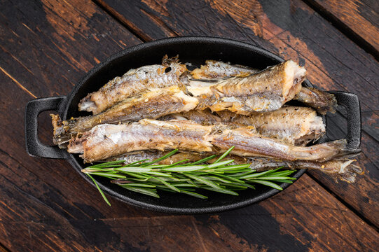 Fried blue whiting resembling small hake and codling served in black pan with fresh rosemary, seafood dish
