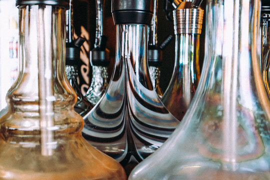 Close up of elegant glass hookah bases with metal stems arranged together, showing reflective surfaces, transparent glass and intricate shapes. Shisha smoking culture, lounge bar atmosphere.