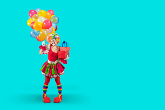 Funny female clown with balloons and gifts, woman entertainer dressed as a colorful Joker in a suit and wig, with clown whiteface makeup. Trickster, jester, pantomime, mime, professional actor