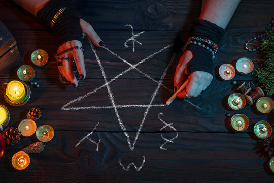 Witch wizard witchcrafting, drawing a pentagram with chalk, casts spell among candles. Magician, Halloween night
