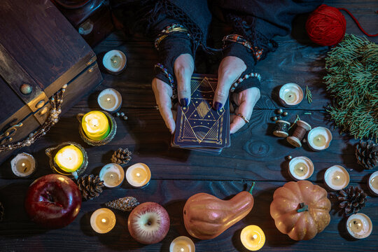 A witch fortune teller casts a spell on Tarot cards among candles and pumpkins. A sorceress on Halloween night.