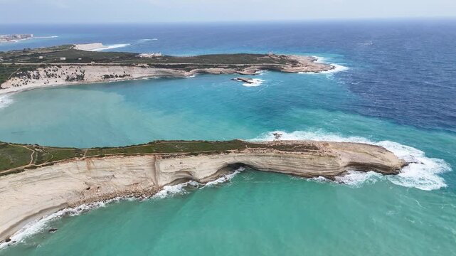 rocky coastal peninsula aerial drone footage malta turquoise coves deep blue open sea sandy beach green scrubland headland distant town skyline mediterranean coastline dramatic seascape panoramic view