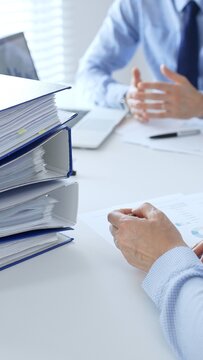 Corporate professionals reviewing financial documents, working collaboratively at white desk with blue folder stack, highlighting teamwork and business productivity. Audit and taxes in business