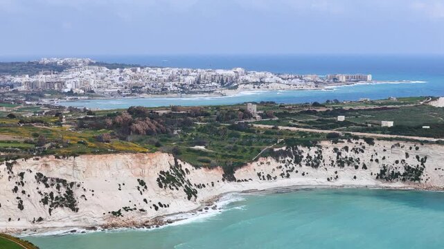 limestone cliff coastal town skyline aerial drone footage malta stone watchtower wildflower fields farmland turquoise bay apartment buildings mediterranean coastal landscape scenic seascape