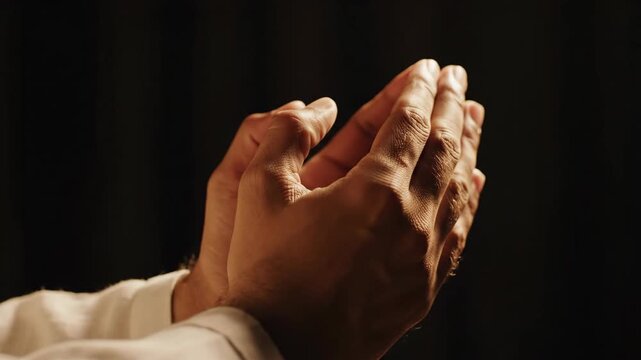 Man's hands clasped in prayer on dark background