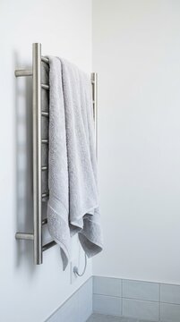 Soft grey towel draped on a modern brushed metal heated towel rail in a bright, clean bathroom with ample copy space