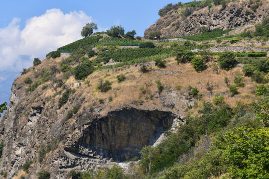 Scenic terraced vineyards on a steep rocky hill over a large mountain cave cliff known as Tetto di Sarre under blue sky, Sarre, Aosta, Italy