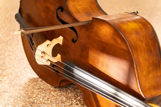 Detailed view of a classic double bass body with a bow resting on the strings. Close-up on the wooden bridge, f-hole, and elegant texture of the stringed orchestra instrument.