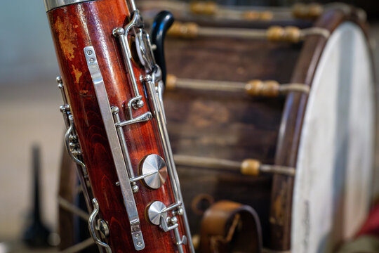 Detailed close-up of a vintage bassoon with silver-plated keys. Traditional wooden drum blurred in the background of a music workshop or studio. Selective focus on woodwind instrument.