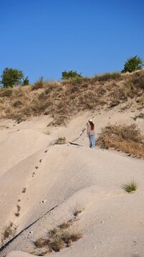 Female traveler slowly walking along sand trail in Cappadocia back view, woman tourist hiking in Love Valley Goreme on volcanic hill, active holiday adventure in Turkey concept.