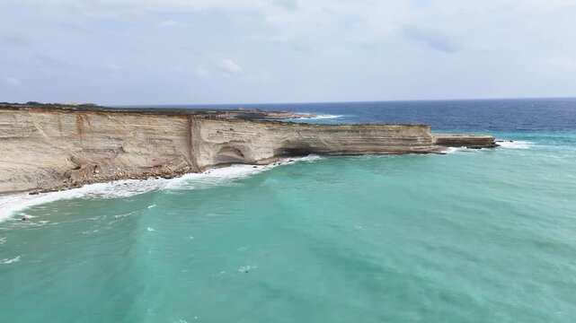 natural rock arch limestone headland aerial drone orbit malta turquoise water sea cave rockfall talus eroded coastline layered rock strata mediterranean coastal geology scenic seascape