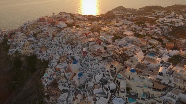 Aerial drone footage of Oia town cliffside architecture and blue dome churches at sunset in Santorini Greece
