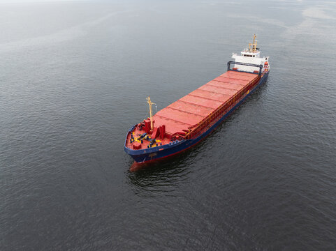 Aerial high angle view of an empty general cargo ship with red hatch covers navigating calm grey waters of the Gulf of Finland in Baltic Sea.