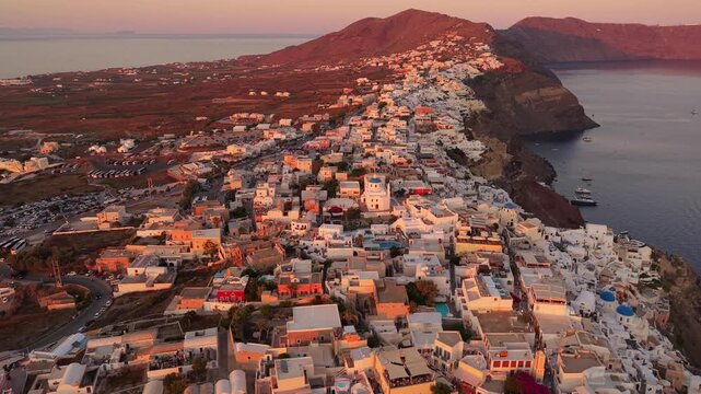 High angle drone of Oia village ridge path and traditional blue dome churches during sunset in Santorini Greece