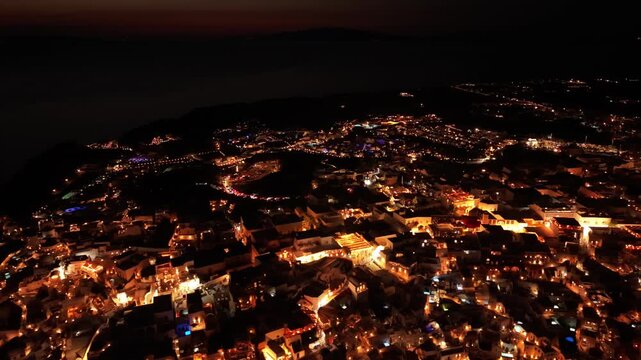 Night drone footage of illuminated Oia village with warm street lights and luxury resorts in Santorini Greece