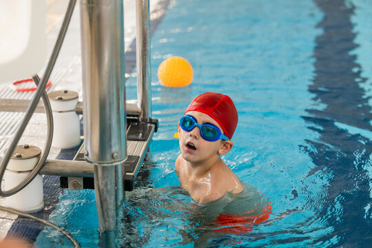 Child with red cap and goggles swimming in indoor pool