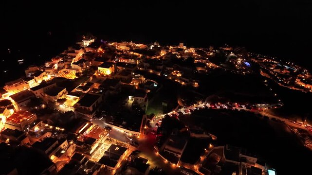 Night drone footage of Oia village streets with car traffic light trails and illuminated windmills in Santorini Greece