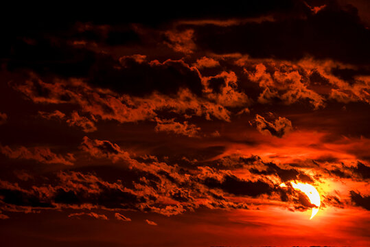 A close-up shot of sunset solar eclipse partially visible through the clouds over the ocean. Beautiful orange sunset partially covered by the moon. 