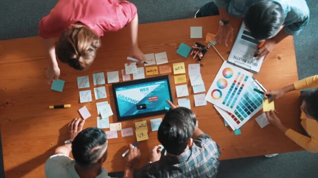Top view of skilled business people working together to design web design. Aerial view of designer brainstorming and discussing about website interface for computer or digital application. Symposium.
