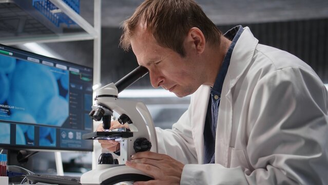 Male scientist investigates tray samples under optical microscope