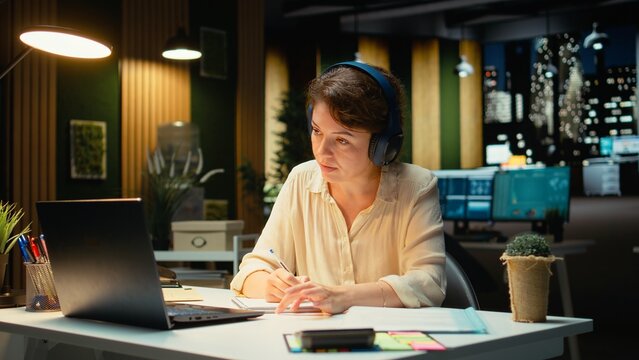 Focused consultant takes notes during an executive board video call extracting key bullet points from a late-night discussion with business associates.