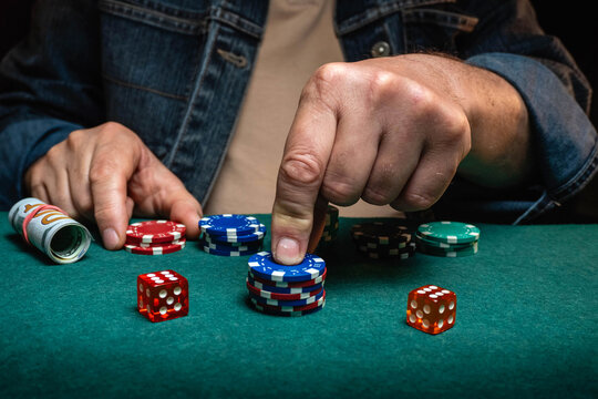 A person is stacking poker chips and rolling dice on a green table. The setting shows a casual environment that suggests a game night among friends