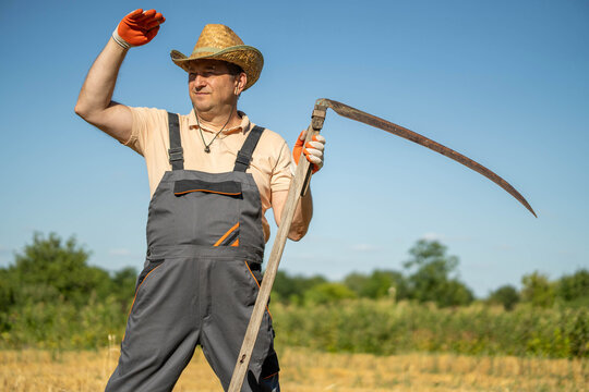 A farmer wearing gray overalls and a straw hat stands in a field holding a scythe. He waves with one hand while the other rests on the tool. The scene shows a clear sky in the daytime