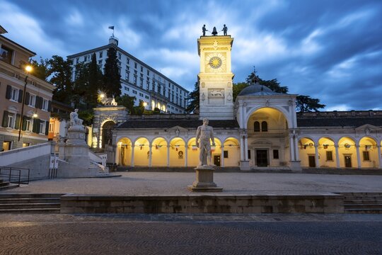 Illuminated main square Piazza della Libert&agrave; with Loggia e Tempietto di San Giovanni and clock tower, Castello di Udine behind, blue hour, dramatic sky, old town, Udine, Friuli-Venezia Giulia, Italy