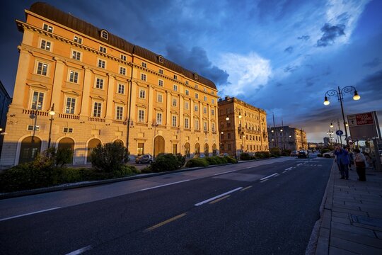 Magnificent buildings on the Riva del Mandracchio seaside promenade in the evening light at sunset, Palazzo della Luogotenenza Austriaca or Palazzo Governo, Greek Orthodox Church of San Nicol&ograve;, dramatic clouds, Trieste, Friuli-Venezia Giulia region, Italy