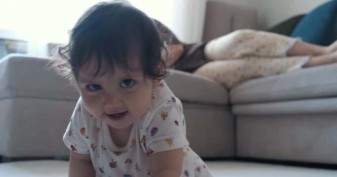 Cute baby girl crawling on living room carpet toward camera and smiling with joyful laughter showing first teeth