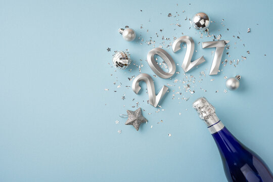 Happy New Year 2027 celebration with silver ornaments, confetti and champagne bottle on blue background