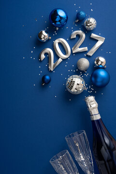 Blue and silver New Year 2027 celebration with champagne bottle, glasses and festive ornaments on vertical navy blue background