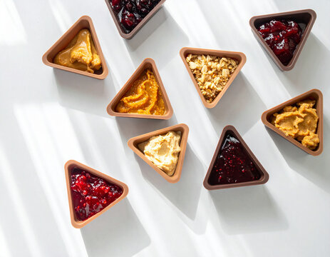 Small triangular silicone snack pods in earth tones are filled with nut butter and jam on a clean table.