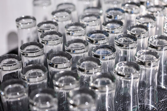 Close-up texture background of multiple clean transparent glass cups placed upside down in neat rows on a rubber mat at a pub or restaurant bar service area, preparing for serving beverages.