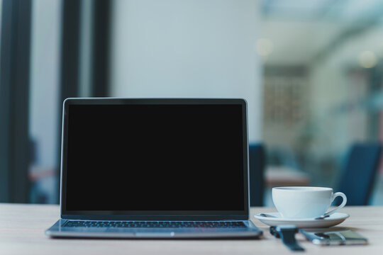 Mockup of laptop computer with empty screen with coffee cup and smartphone on table of the coffee shop background