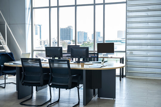 empty co-working space Modern office workspace with office chairs, and two computers with blank white screens for mockup, set against big glass windows overlooking a blurred cityscape.