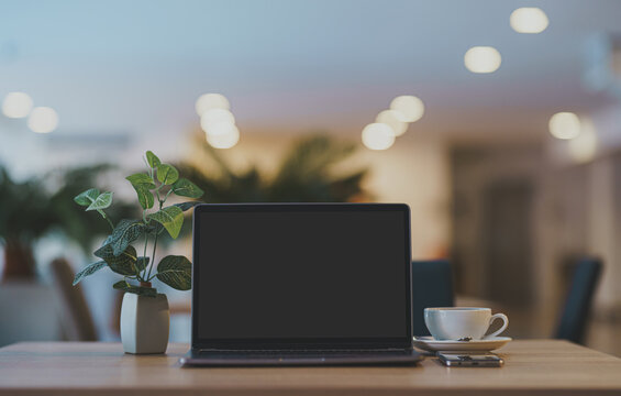 Mockup of laptop computer with empty screen with coffee cup and smartphone on table of the coffee shop background