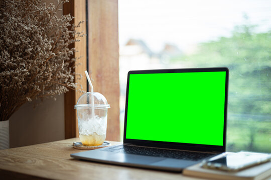 Mockup of laptop computer with empty screen with coffee cup and smartphone on table of tree branch shadow the cafe coffee shop background,Green screen