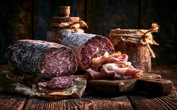 Artisan cured meat slices, traditional charcuterie and gourmet food production, rustic wooden table in a dark warehouse setting