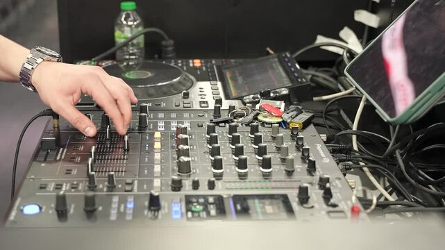 Close-up of DJ hands mixing music on professional sound console mixer and turntable in nightclub