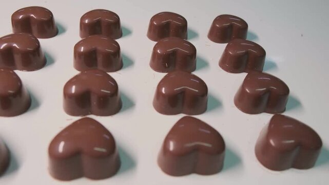 Close-up of melted liquid chocolate pouring over confectionery candies on automated conveyor belt in factory