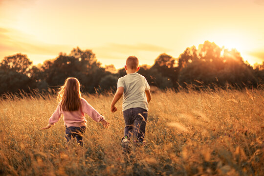Carefree Brother and Sister Running Through Golden Meadow at Sunset