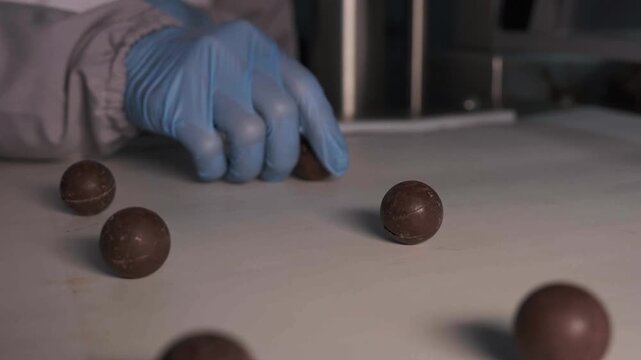 Close-up of melted liquid chocolate pouring over confectionery candies on automated conveyor belt in factory